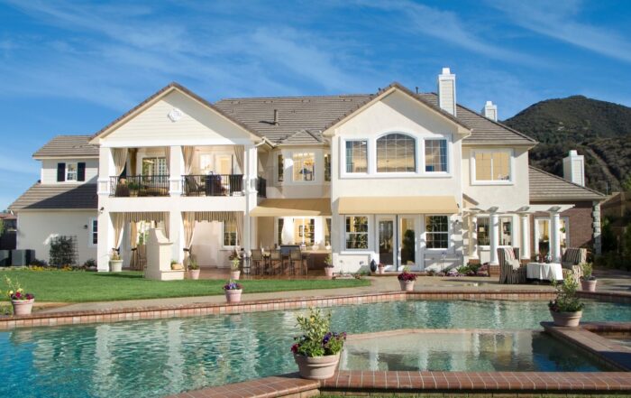 Investment properties white two-story house with a pool in the foreground and mountains in the background.