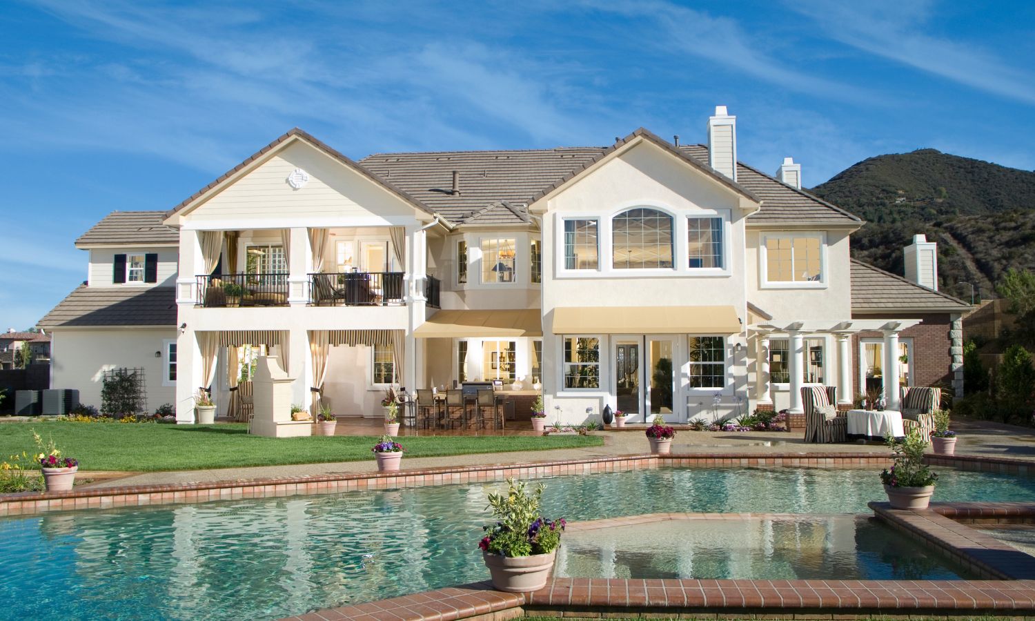 Investment properties white two-story house with a pool in the foreground and mountains in the background.