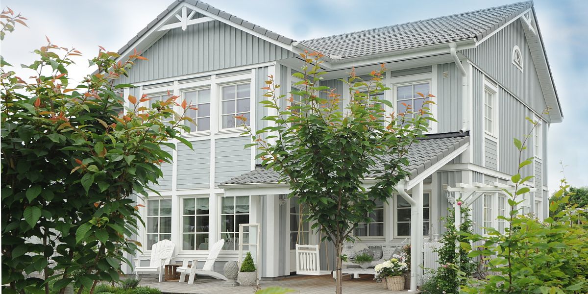 Light blue two-story house with white trim surrounded by trees and a small garden.