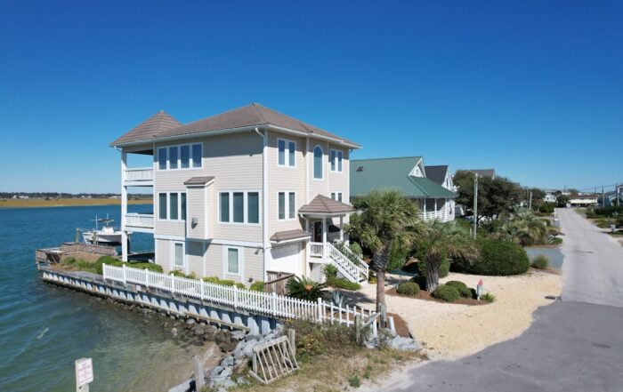Exterior of a modern luxury waterfront home with large windows and a swimming pool, bathed in bright, warm sunlight.