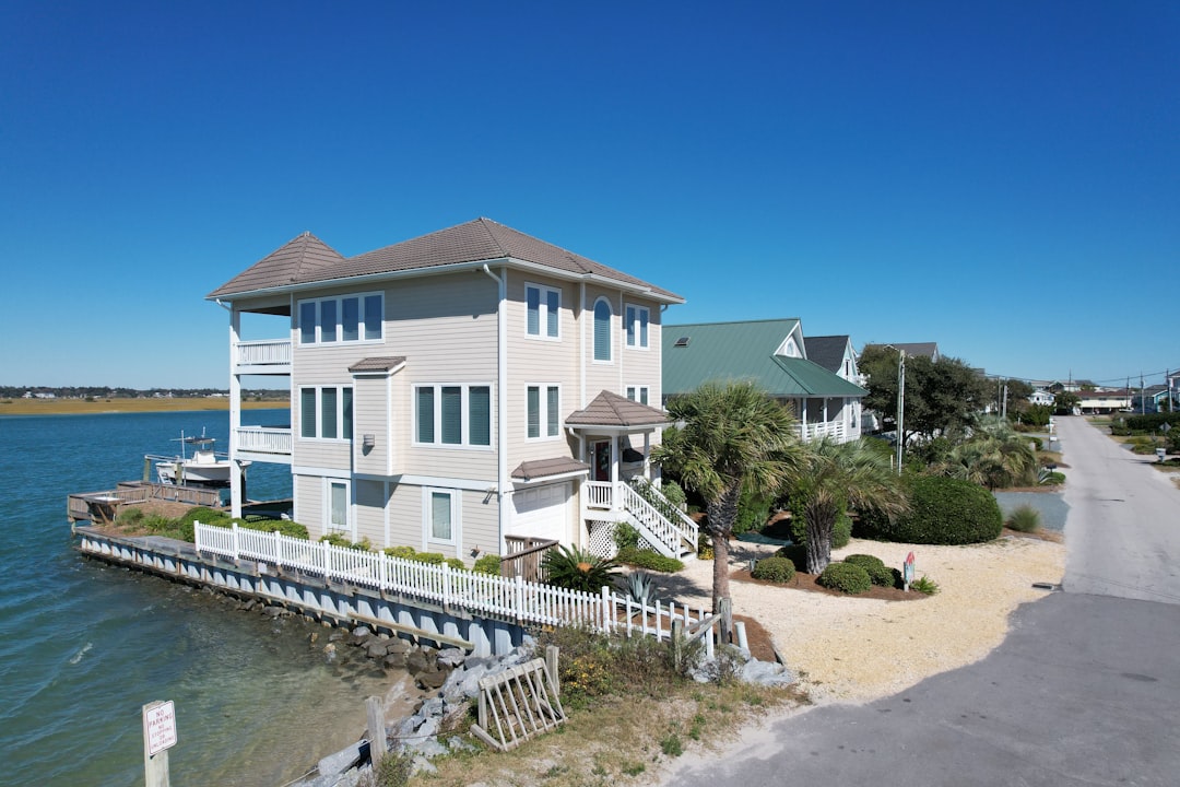 Exterior of a modern luxury waterfront home with large windows and a swimming pool, bathed in bright, warm sunlight.