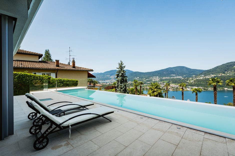 A sophisticated person holding a tablet that displays a virtual tour of a luxurious modern home, symbolizing an international buyer engaging with a digital property listing.