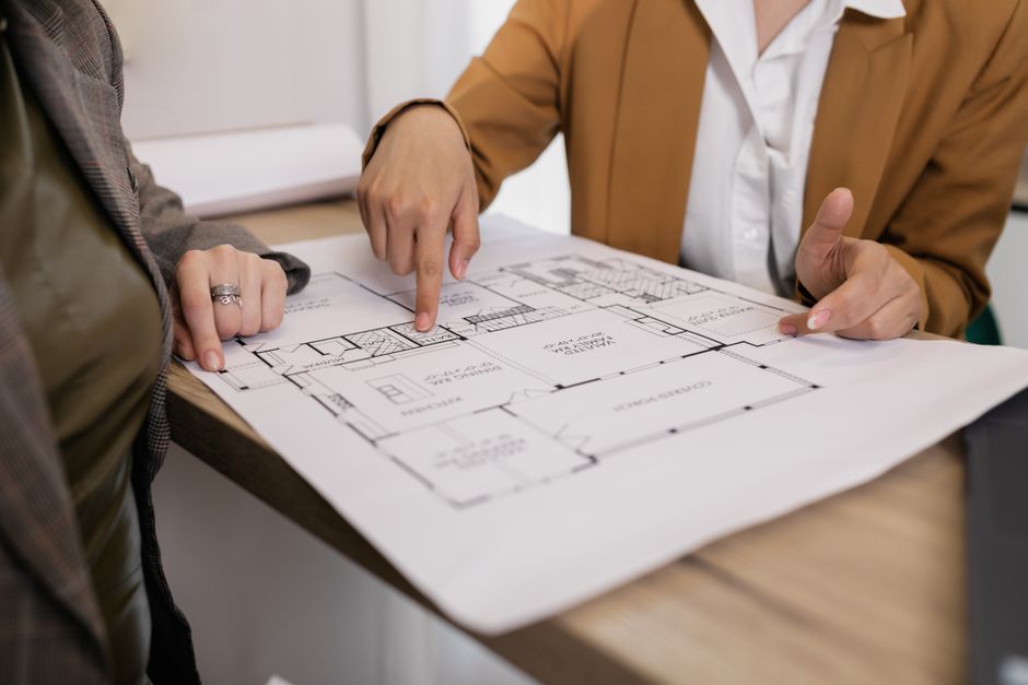 Two well-dressed professionals in a bright, contemporary office setting collaborating over architectural plans, representing the strategic expertise and high-level service involved in a million-dollar sale.
